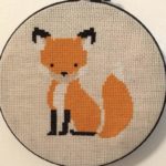 Cross stitched orange fox in black embroidery hoop with cream background
