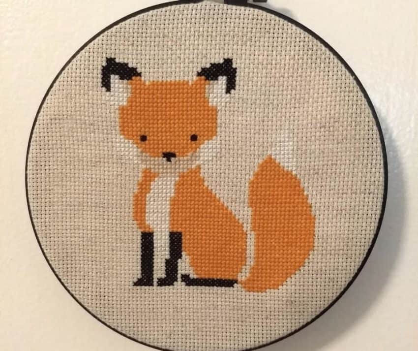 Cross stitched orange fox in black embroidery hoop with cream background